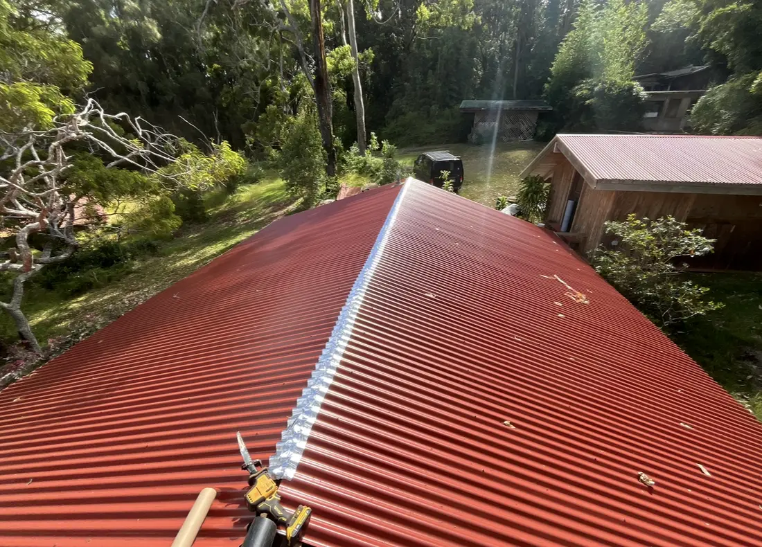 A finished red metal roof over the property, trees behind